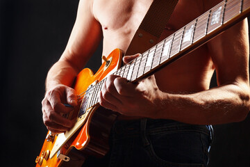 Rock guitarist with sunburst orange electric guitar on dark stage.