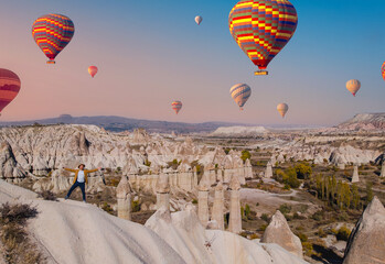 Aerial view of beautiful stone pillars and hot air balloons in love valley with man tourist...