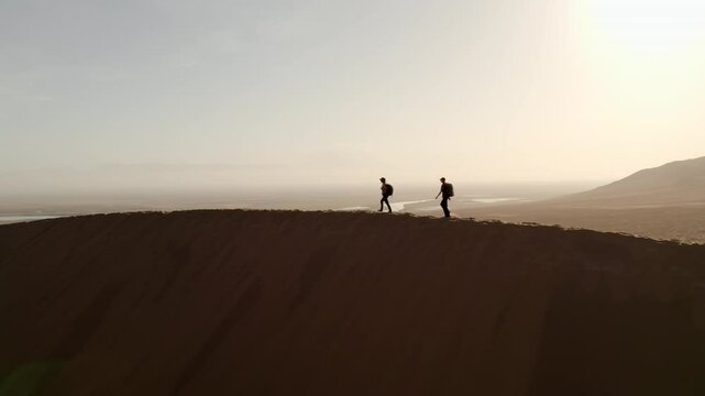 Two girls with big backpacks walking on top of a dune with a river valley in the background in the Altyn Emel national park, Kazakhstan