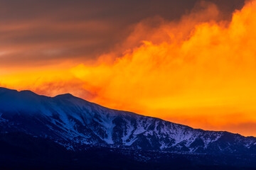 beautiful orange mountain sunset with highland slope in snow and amazing cloden eveninf clouds on...