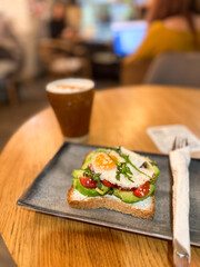 Avocado toast with egg served on a ceramic plate in cozy cafe. Healthy breakfast and balanced nutrition in a lifestyle setting.