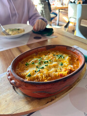 Baked pasta served in clay dish on wooden board. Conveys warmth, tradition, and the comfort of a hearty homemade-style meal in a cozy setting.