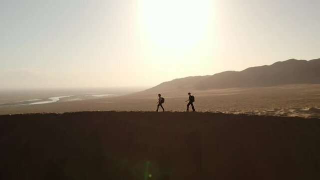 Aerial view of two tourists walking at sunset against the backdrop of the martian landscape of the Altyn Emel national park, Kazakhstan