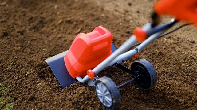 Woman preparing garden beds for planting using cultivator. Rotovator, garden tiller, rotary tiller close up. Cultivators break up compacted soil, improve its structure and aeration.
