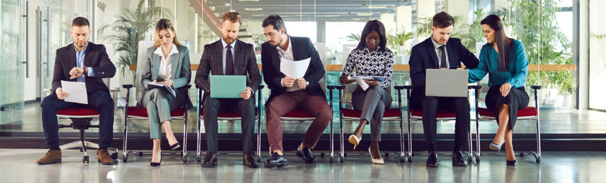 Group of candidates sits in a row at an office, waiting for job interview. The business environment creates a professional setting as the people prepare for the work related opportunity.