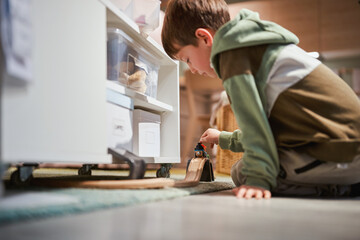 Curious young boy playing with a wooden train on a track at home