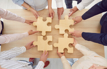 Top view of people hands assembling big wooden puzzle standing in circle in office. Coworkers join...