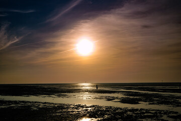 Obraz premium Ein sonniger Frühlingstag geht zu Ende und die untergehende Sonne steht schon tief über dem Wattenmeer bei Sahlenburg, Deutschland.