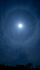 Bright moon shining through winter sky with lunar halo and stars