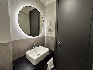 Modern bathroom with round mirror and stylish sink in contemporary hotel. Cleanliness, comfort,...