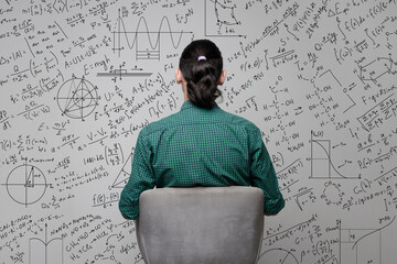 A woman is sitting near a wall with a drawing of mathematical equations, graphs amd diagrams. Idea...