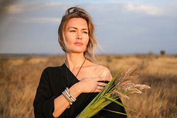 A radiant young woman smiles softly against a wild nature and evening summer sky.