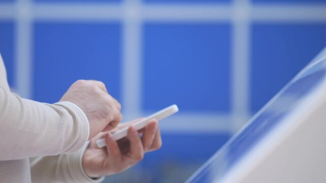 Person is using a cell phone with a blue background. The person is looking at the screen and he is focused on the content. The blue background adds a sense of calmness and serenity to the scene