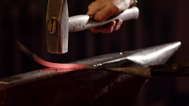 Closeup of a red hot glowing iron being hammered on an anvil, slow motion