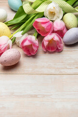 Easter eggs and pink and white tulips lying on a wooden surface