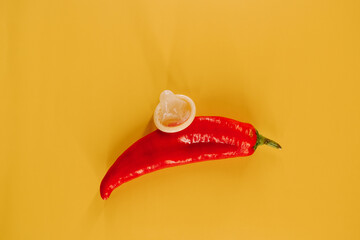 Chili pepper with a condom on yellow backdrop for a creative illustration