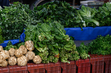 Fresh herbs and vegetables displayed on a stall at a farmers market. Bunches of parsley, dill, and lettuce mix with tomatoes, cucumbers, and peppers, creating a vibrant and healthy selection.