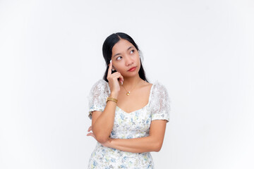 Unsure young Southeast Asian woman thinking with hand on temple feeling uncertain while in white...