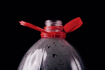 Close up of new cap attached to plastic bottle, isolated on black background. Environmental...