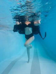 A woman is swimming in a pool wearing a black dress and a black bikini top