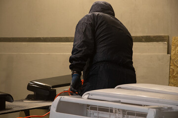 Painter paints the air conditioner housing from a paint sprayer in the workshop, painter, painting