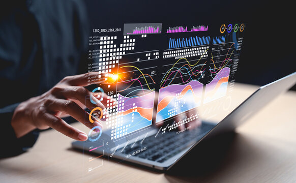 A hand interacts with holographic data visuals above a laptop, showcasing modern technology and data analysis.