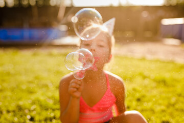 Girl blowing soap bubbles outdoors at sunset, surrounded by golden sunlight