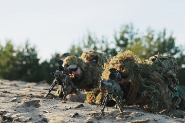 Camouflaged military men in moro uniforms wear ghillie suits covered in grass, staying concealed in the field, preparing for tactical operations and enemy surveillance.