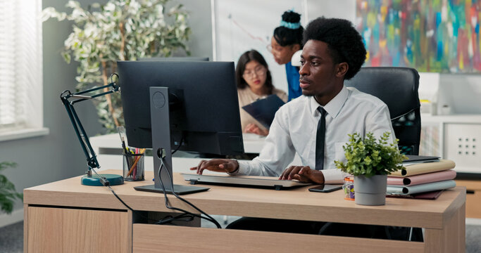 An experienced handsome company employee dressed in a shirt and tie prepares documents on the computer, drafts an article or a speech, sends messages to clients, taps fingers on the keyboard
