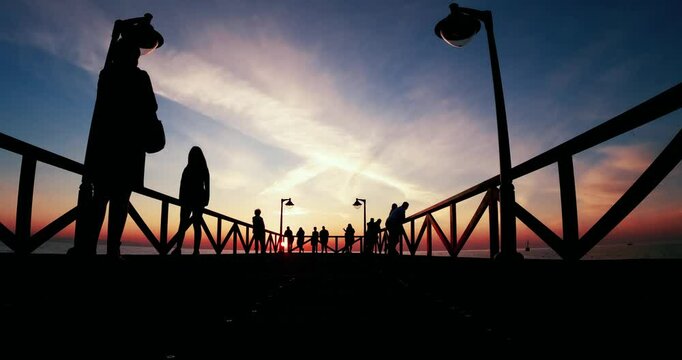 Silhouettes of people enjoy view on pier during a serene sunrise