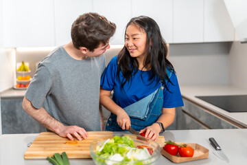 Multiethnic couple preparing fresh salad together at home