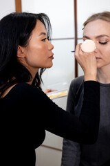Professional makeup artist carefully applying eyeshadow to a young woman in a beauty salon. The setting is bright and modern, showcasing a beauty treatment in progress.