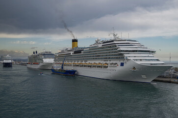 Modern cruiseship cruise ship liner Favolosa docked in Barcelona, Spain with bunker fuel vessel  and coast line beautiful landscape scenery and city skyline during Mediterranean cruising