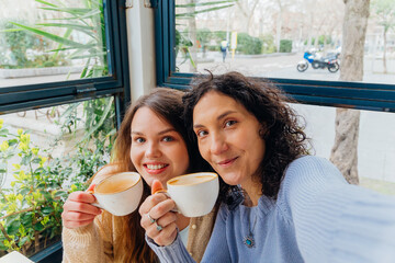 Mother and daughter smiling and holding coffee cups in cafe