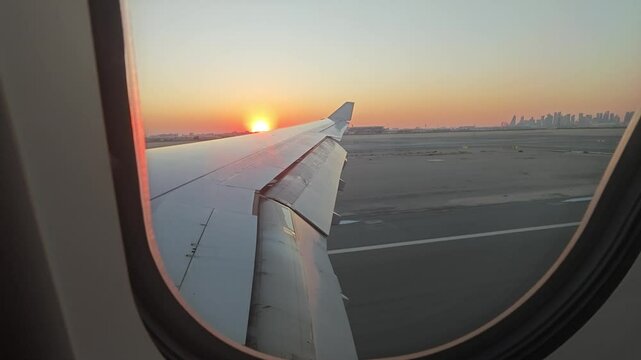 Airplane wing view landing over Doha airport at golden hour, Qatar