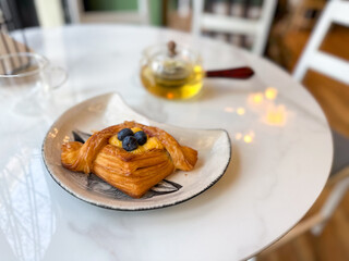 Blueberry pastry with tea served on white marble table. Represents comfort, calm, and sweet daily rituals in a cozy cafe atmosphere