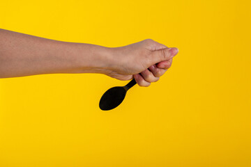 Hand and black spoon on yellow background.