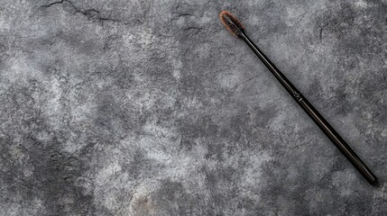 Black Mascara Wand with Brown Bristles on a Textured Gray Surface
