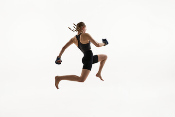 Dynamic image of young woman, Thai boxing athlete in high jump with boxing gloves, fierce focus and motion in frame. Concept of sport, MMA, strength, combat sport, strength, endurance