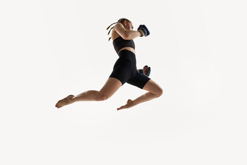 Low angle view of woman captured in high jump with boxing gloves, fierce focus training against...