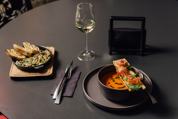 Salmorejo soup - Spanish tomato puree soup with a rich flavor of roasted vegetables such as bell pepper and shallots, enriched with cream and butter. Minimalistic dining scene with a glass of wine