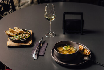 Chicken soup with egg noodles, spinach, broccoli and parmesan croutons. Minimalistic dining scene with a glass of wine, copy space
