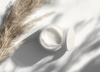 Fototapeta premium open jar of cream with white texture, dry grasses and shadows on a light background, minimalist mockup for cosmetic product presentation, aesthetic composition, flat lay, studio photography