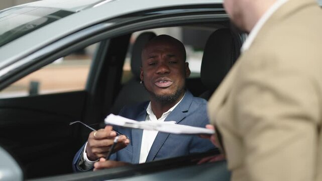 An auto dealer consults and signs an agreement to lease or buy a new car with a black businessman at a car dealership. The concept of buying, leasing and insuring a car. 