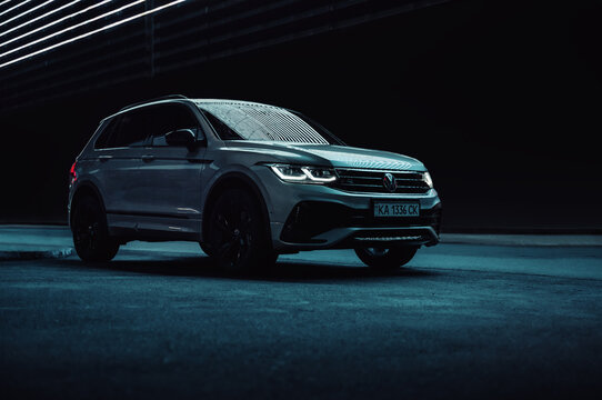 Volkswagen Tiguan on dark city street at night. Front three quarter view of modern SUV at night, glowing LED lines above in the background. Kyiv, Ukraine - September 19 2021.