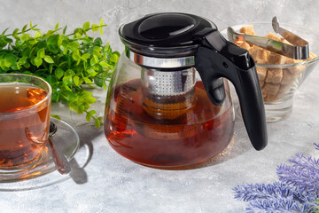 Glass teapot with metal strainer inside. Kitchen utensils on gray background.
