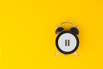 Black alarm clock with pause sign on yellow background including copy space, for take a break, overworked concept, hormone replacement therapy