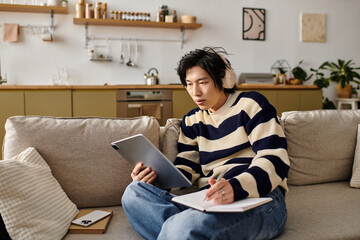 Obraz premium Handsome young asian man immersed in online learning while relaxing at home