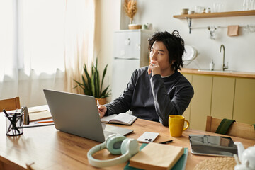 Young asian man engaged in online learning at home while taking notes and reflecting