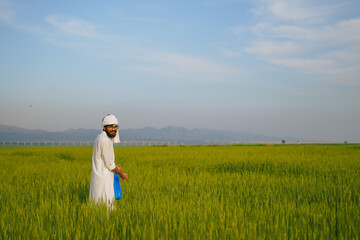 A smiling farmer wearing traditional white clothing and a headscarf stands in a lush green wheat...